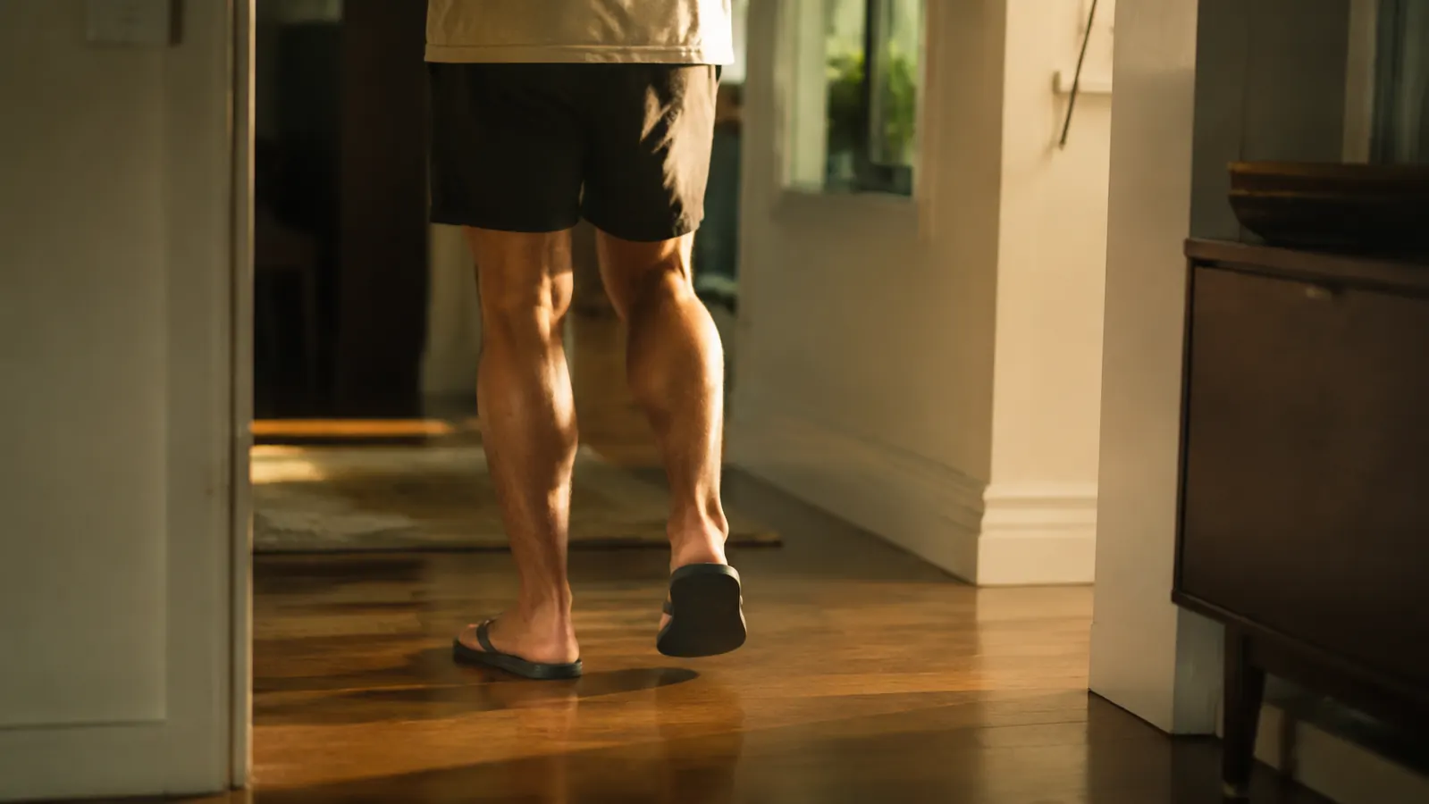 A person walking across a hardwood floor at home in recovery sandals, casual evening setting